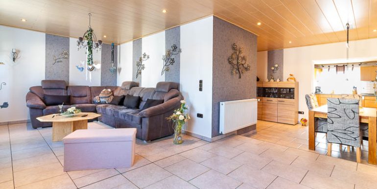 Stilvoll eingerichtetes Wohnzimmer mit großer Polsterecke, dekorativen Wandobjekten und Blick zur Wohnwand.